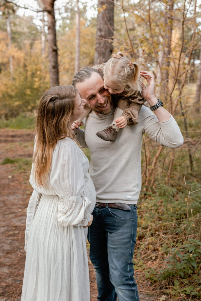 Fotoshoot van een gezin met zwangere mama in een prachtig gekleurde herfstsetting op speelse wijze.