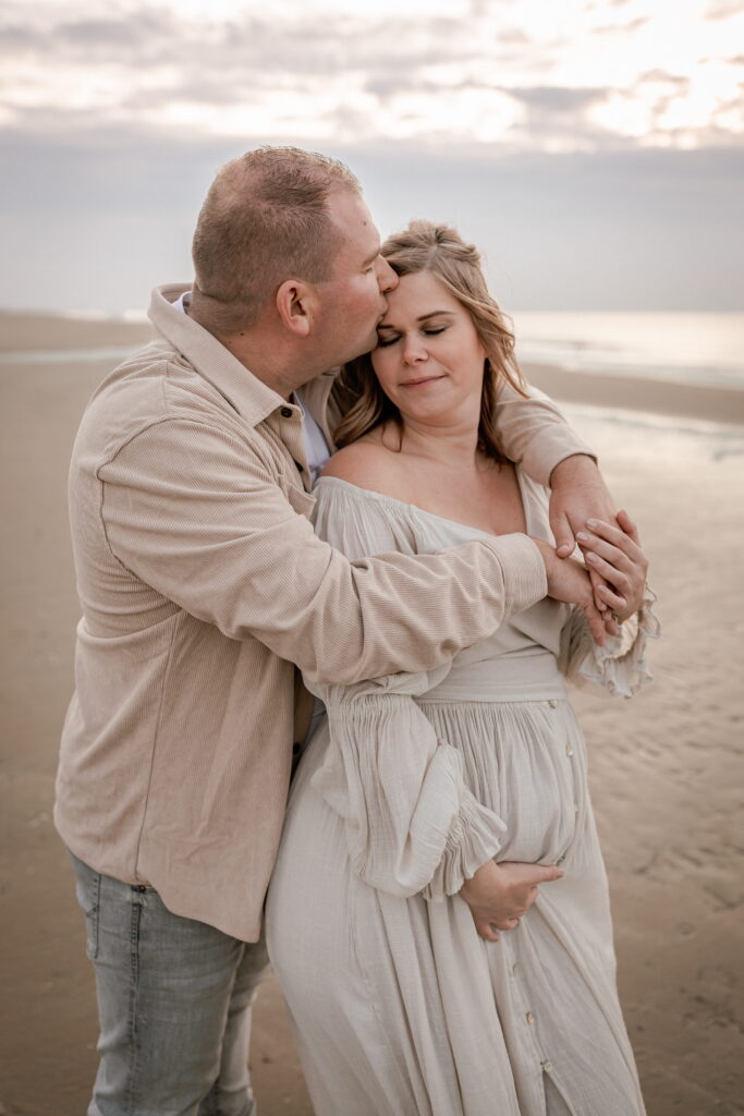 Liefdevol koppel tijdens een ongedwongen zwangerschapsshoot op het strand van Noordwijk.